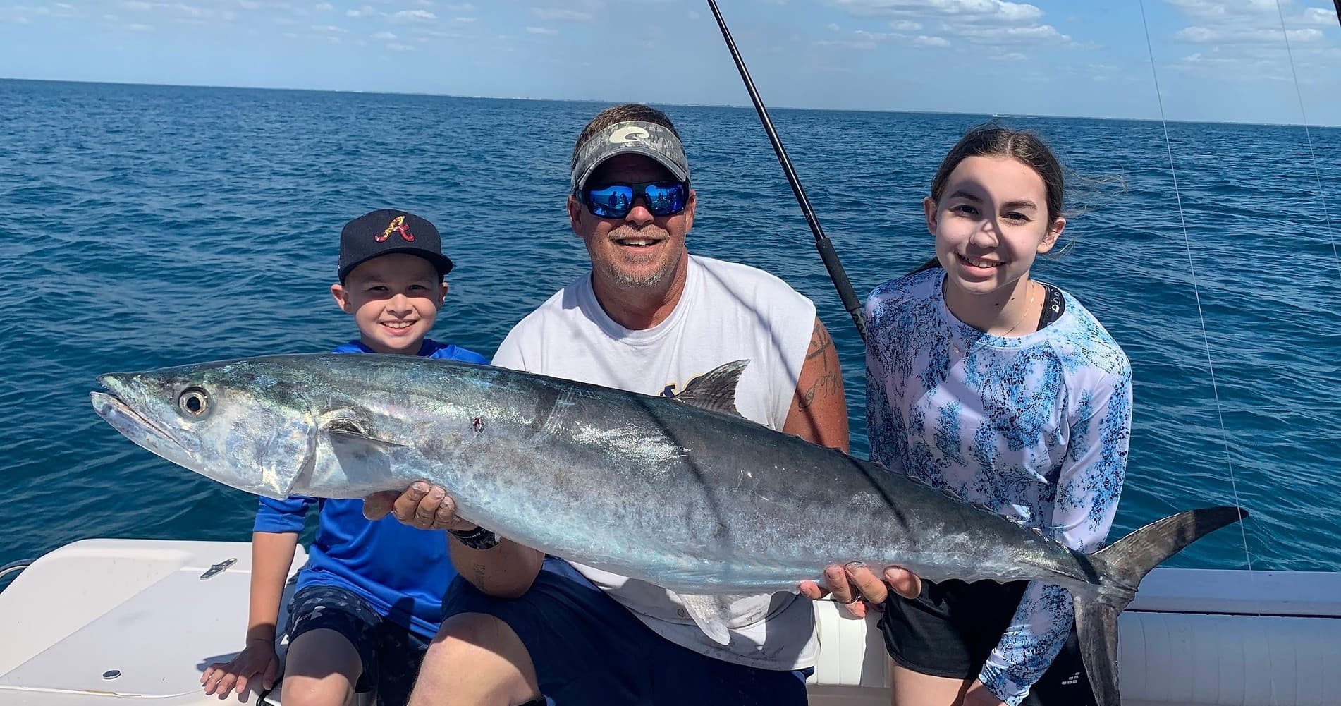 Family holding large offshore wahoo on boat with open ocean
