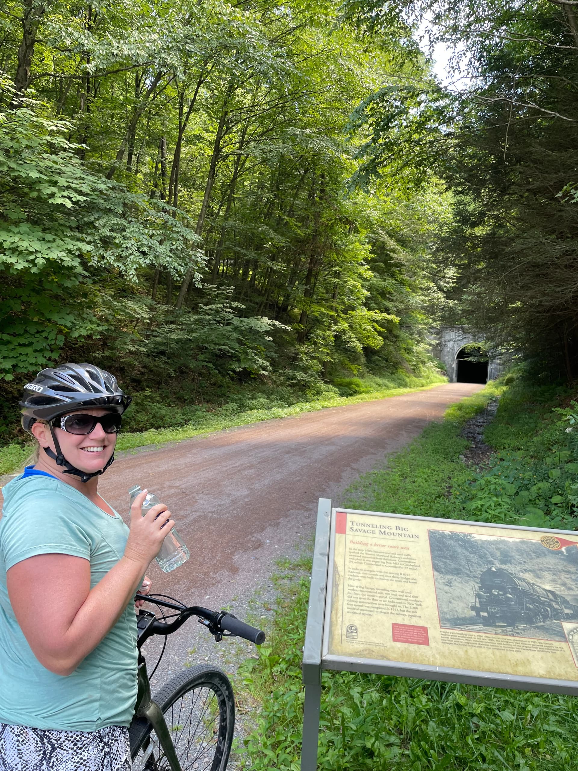 Cyclist pausing on shaded forest rail-trail near tunnel