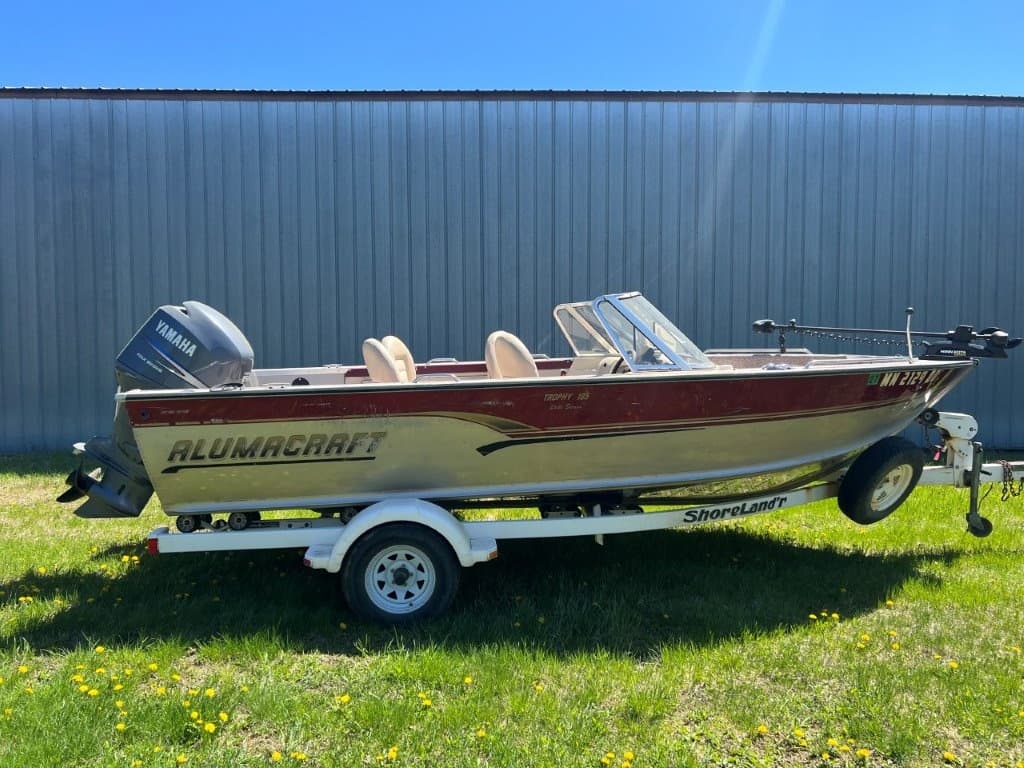 Aluminum fishing boat on trailer parked on grassy lot