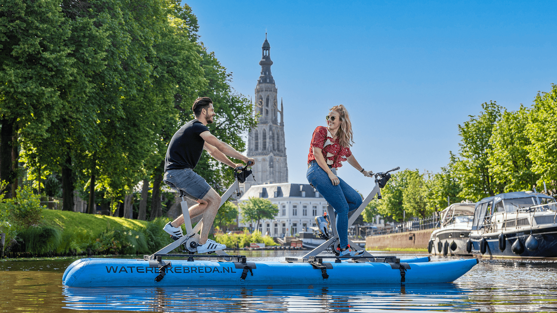 Pair pedaling waterbike on sunny canal with historic church view