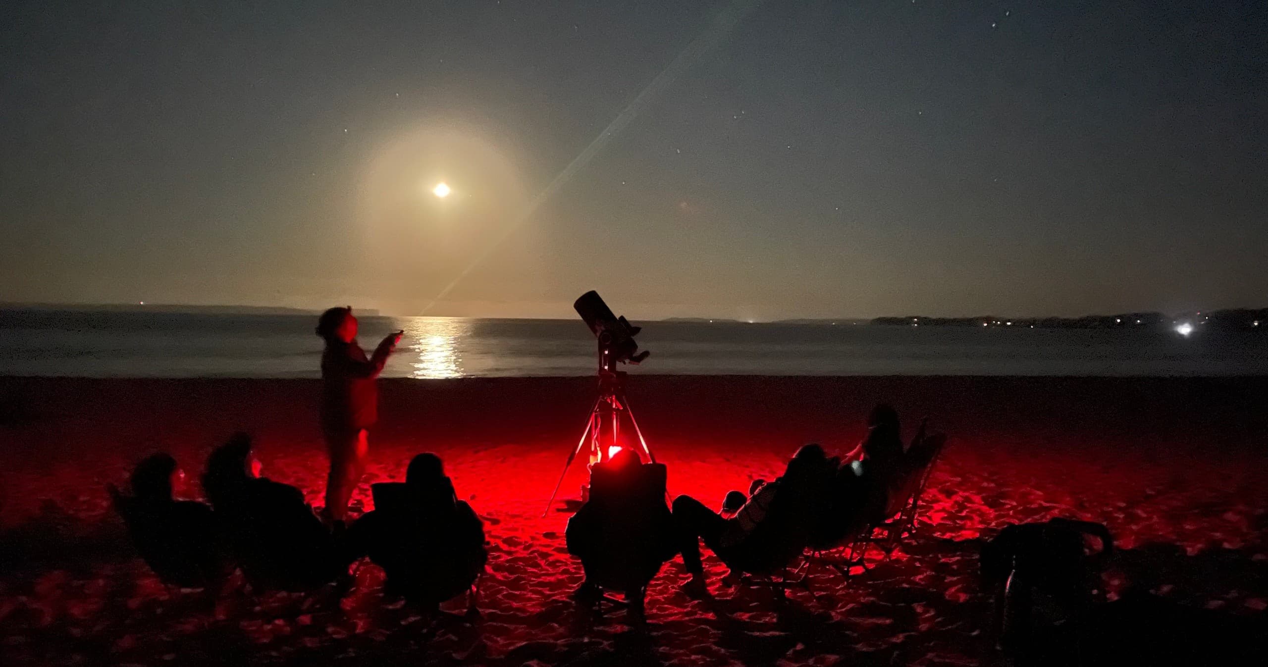 Moonlit beach stargazing with telescope and red lights at shore