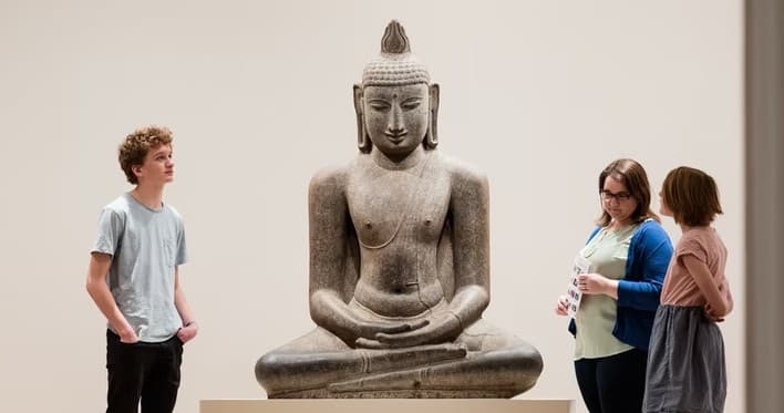Large seated Buddha sculpture in museum gallery with visitors