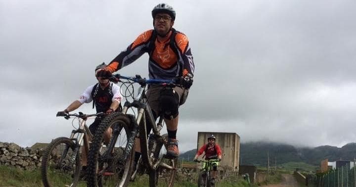 Mountain bikers riding rugged trail with dramatic cloudy hills