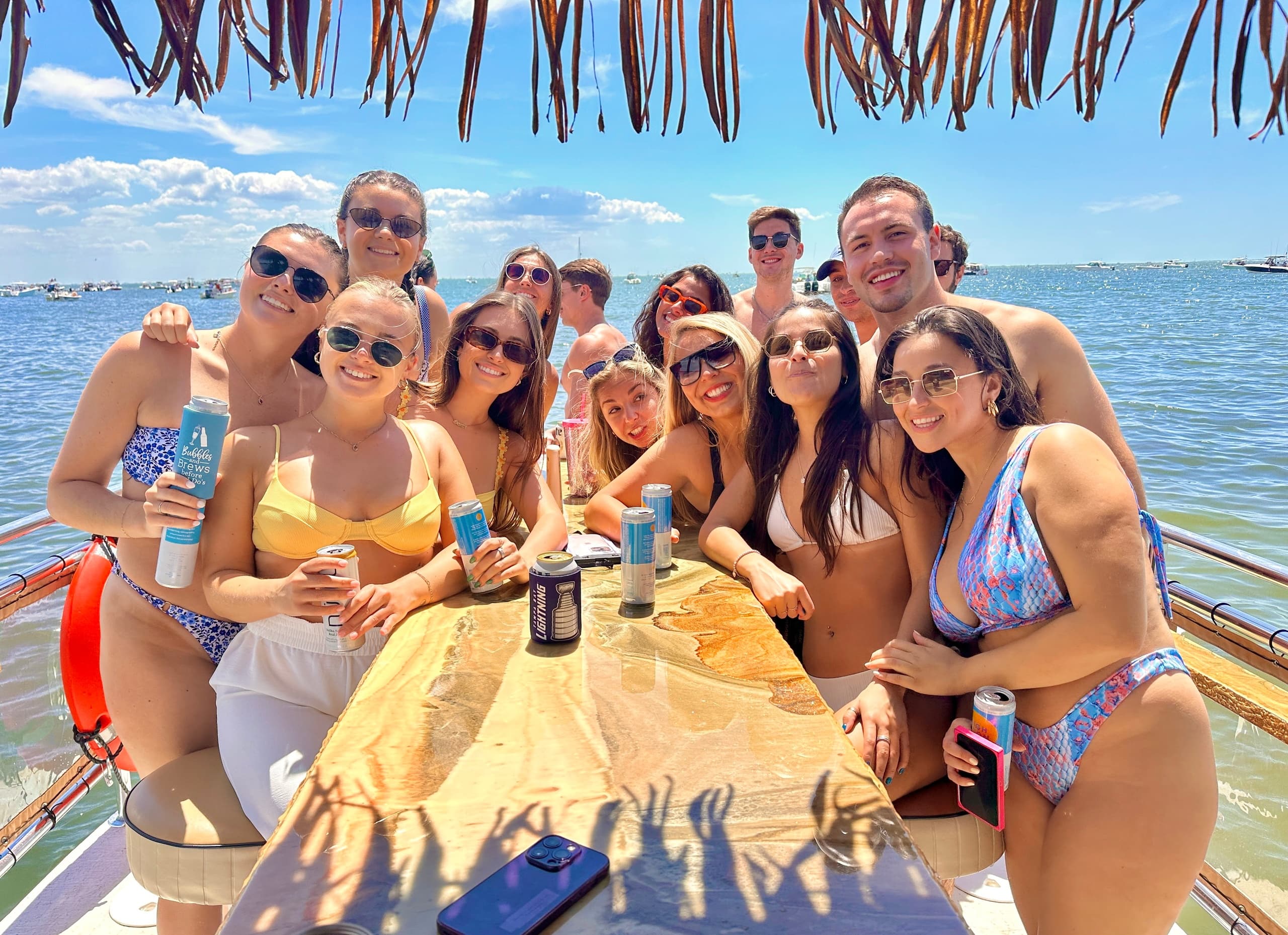 Friends drinking at boat table under palapa with bay and bridge