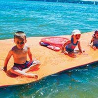 Children playing on large floating orange water mat in ocean