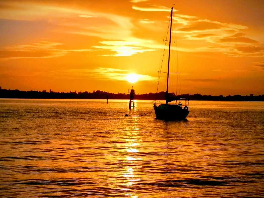 Sailboat silhouetted at golden sunset over river harbor