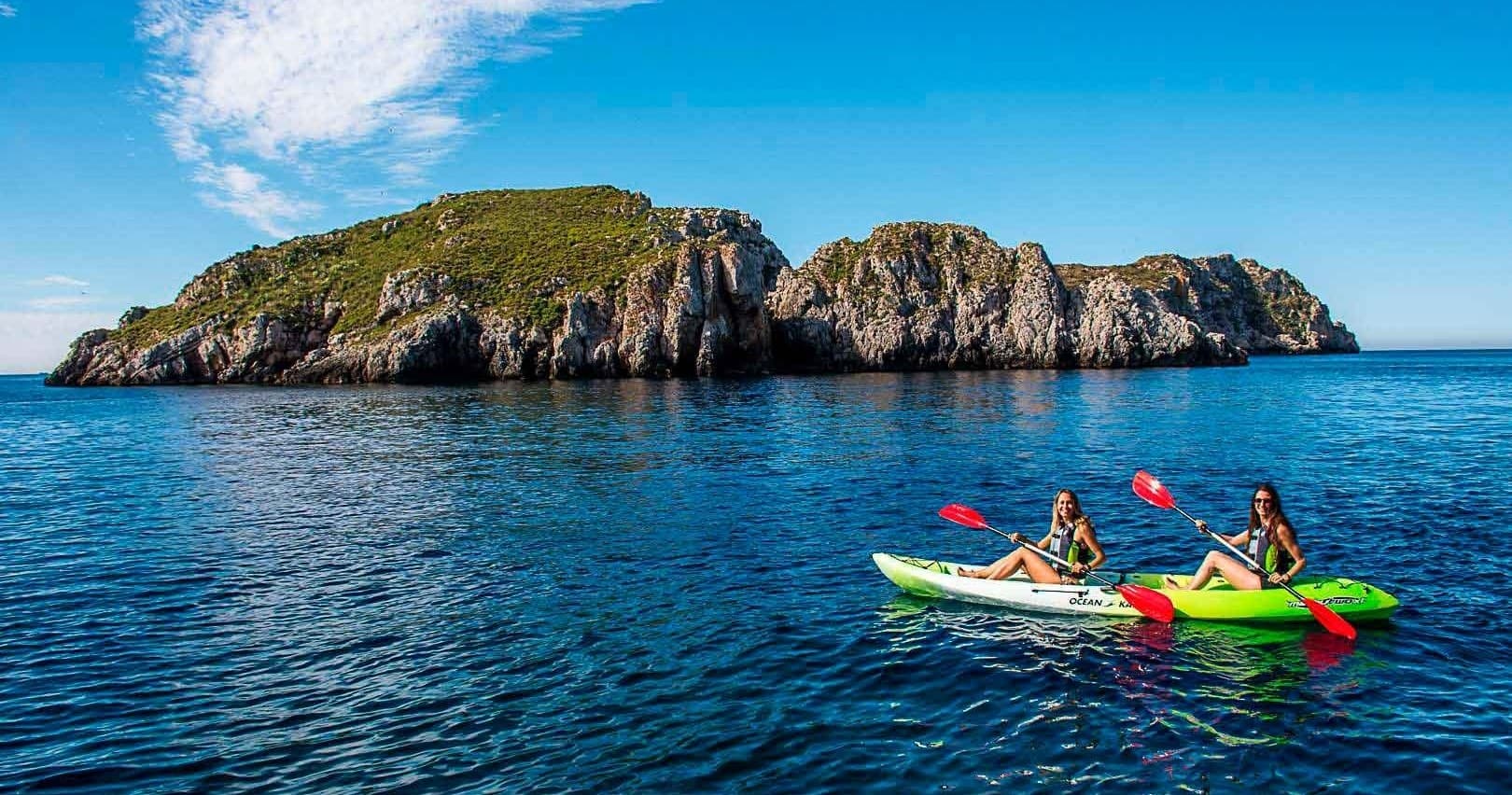 Kayakers paddling near rocky island in clear Mediterranean