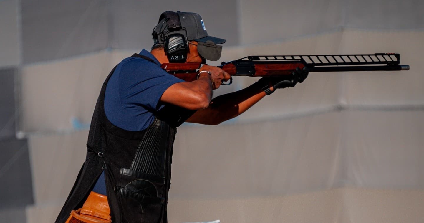 Competitive shooter aiming a shotgun at outdoor clay range