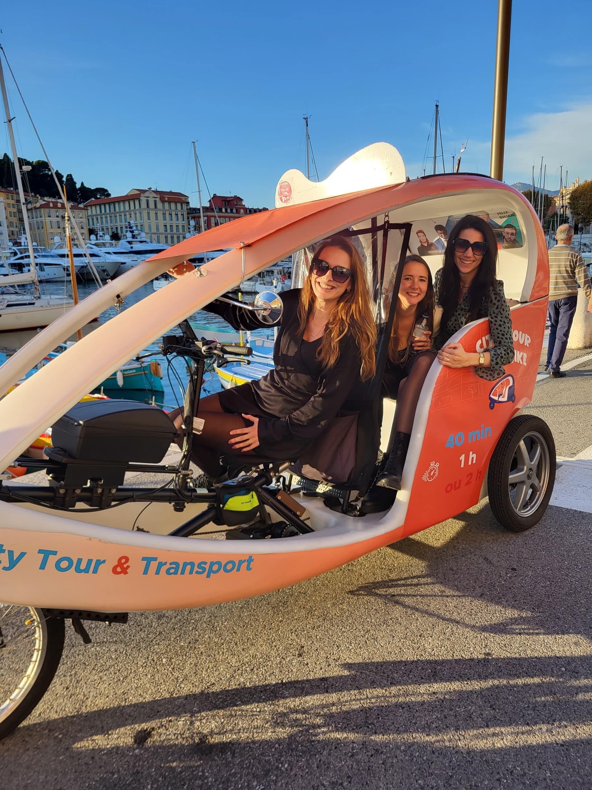 Women seated in orange pedicab parked at marina waterfront sunset