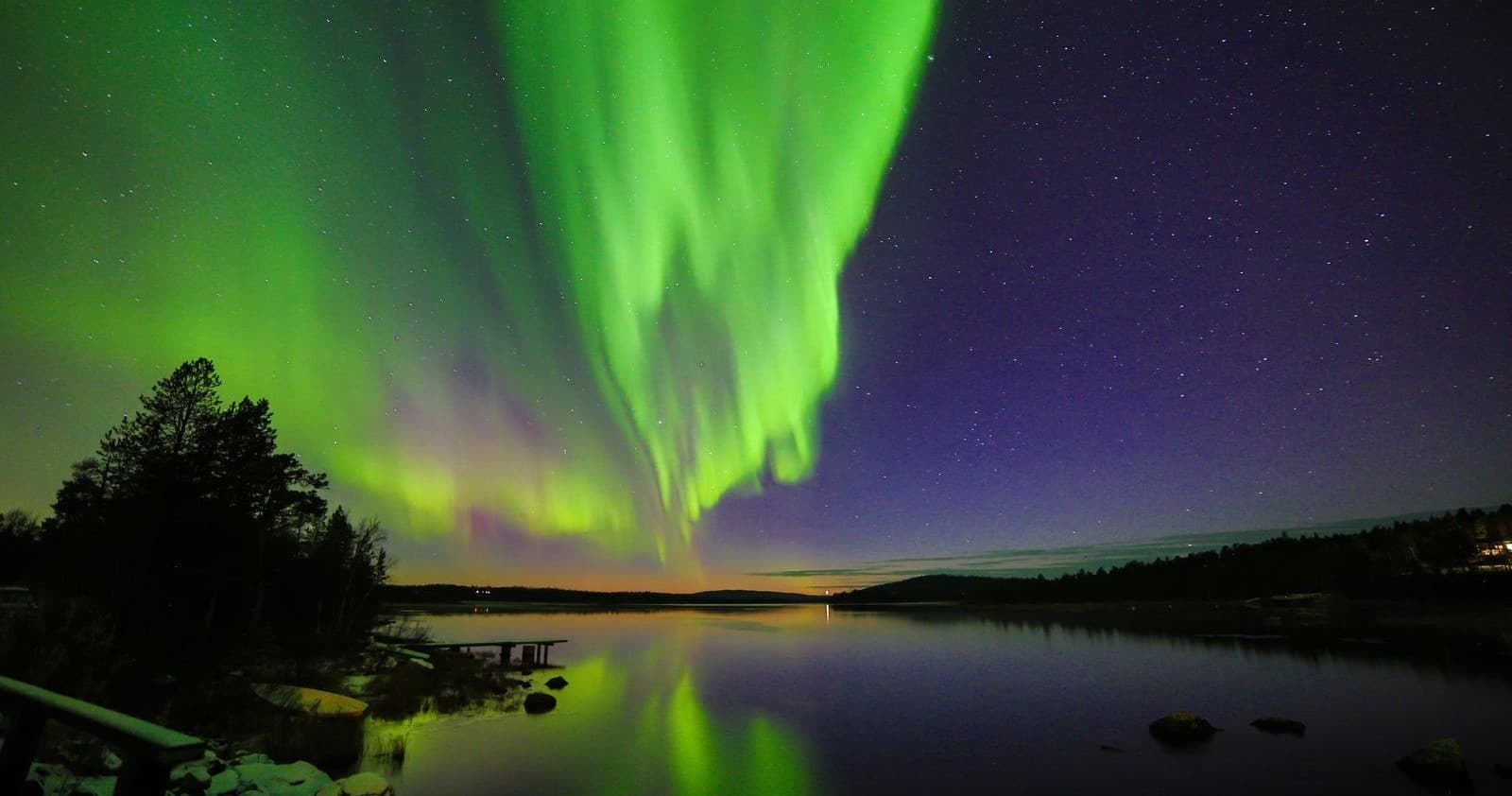 Vibrant northern lights over treeline and lake, Lapland night