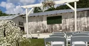 Rustic outdoor ceremony pergola with white chairs at farm venue