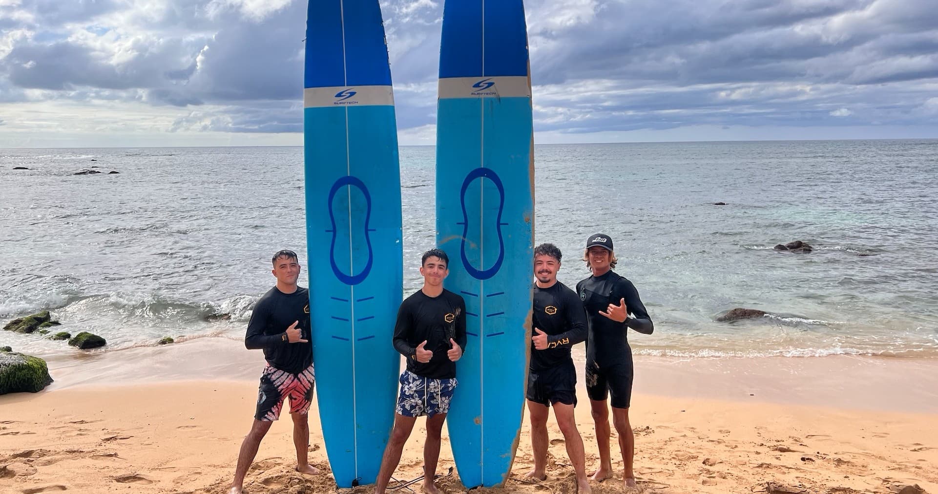 Surf instructors posing with twin blue boards on rocky beach