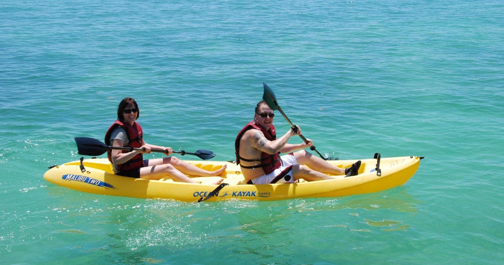 Two kayakers paddling a yellow tandem kayak in clear sea