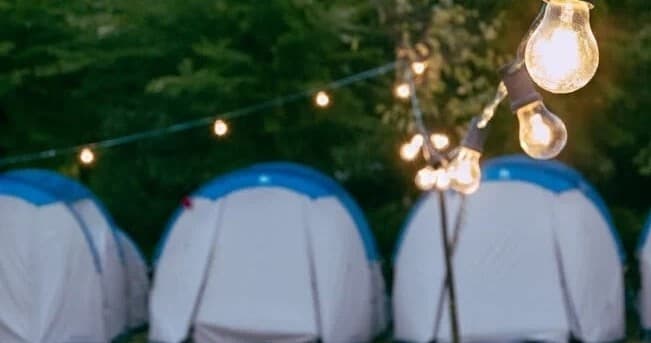 Campsite tents lit by string lights, evening glamping setup
