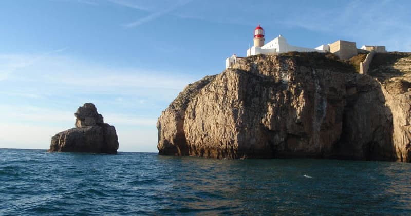 Coastal lighthouse on rugged cliffs overlooking calm ocean horizon