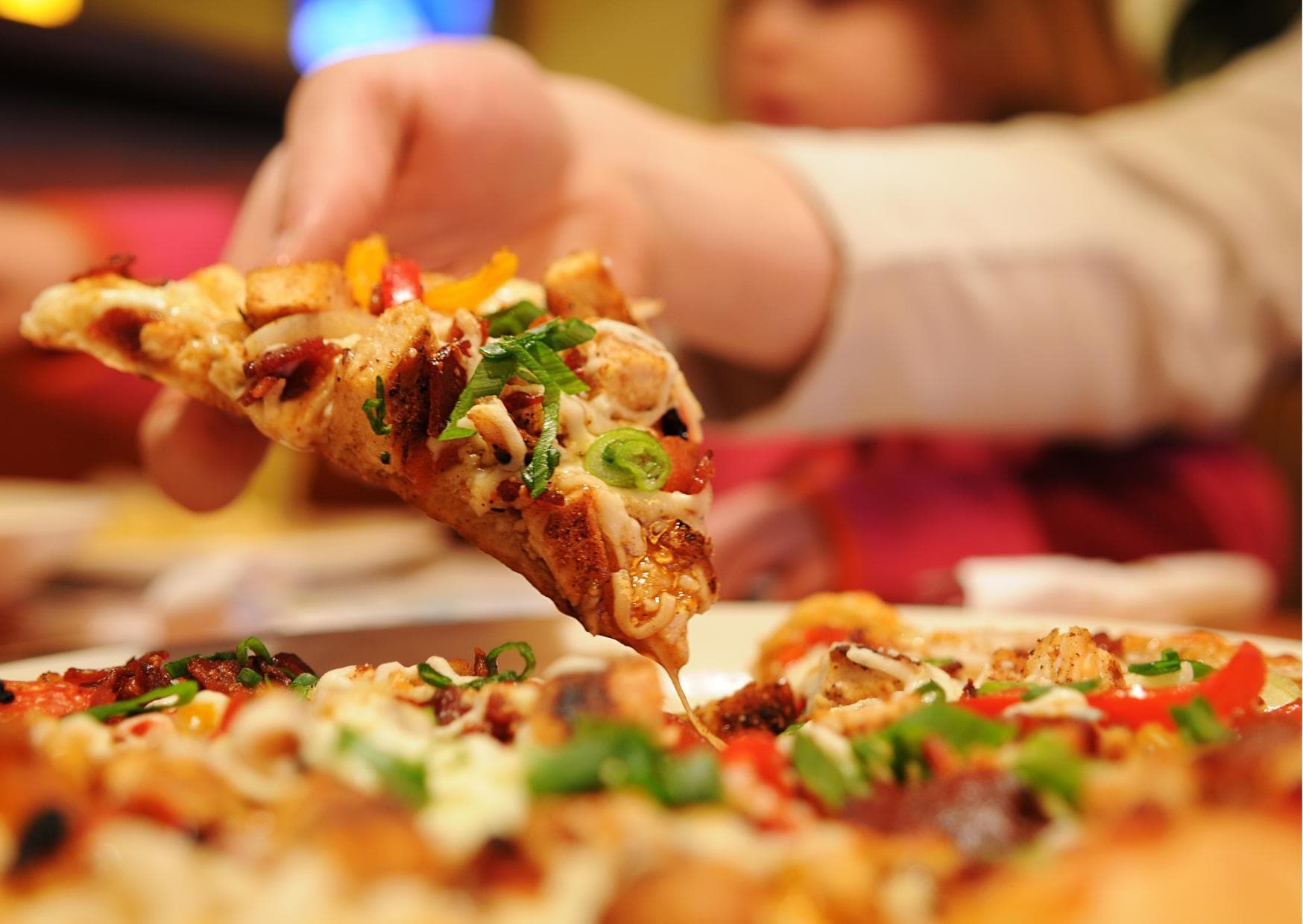 Hand pulling hot pizza slice with toppings at casual dining table
