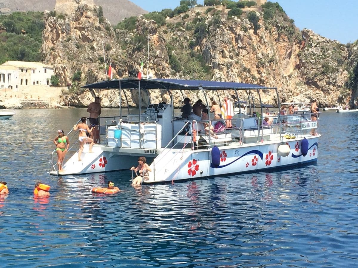 Tour boat anchored by rocky Mediterranean coast with swimmers