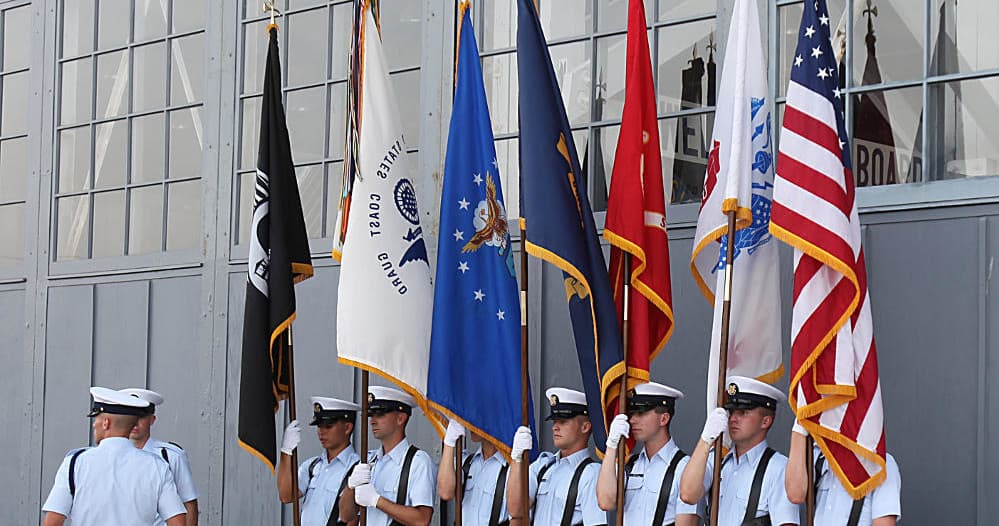 Honor guard carrying flags at airfield ceremony outside hangar
