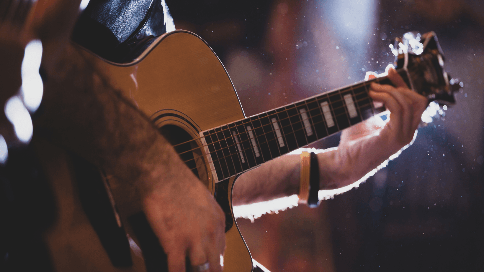 Folk musician strumming acoustic guitar on dimly lit indoor stage