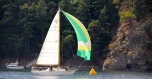Yacht with colorful spinnaker racing near rocky forested shore