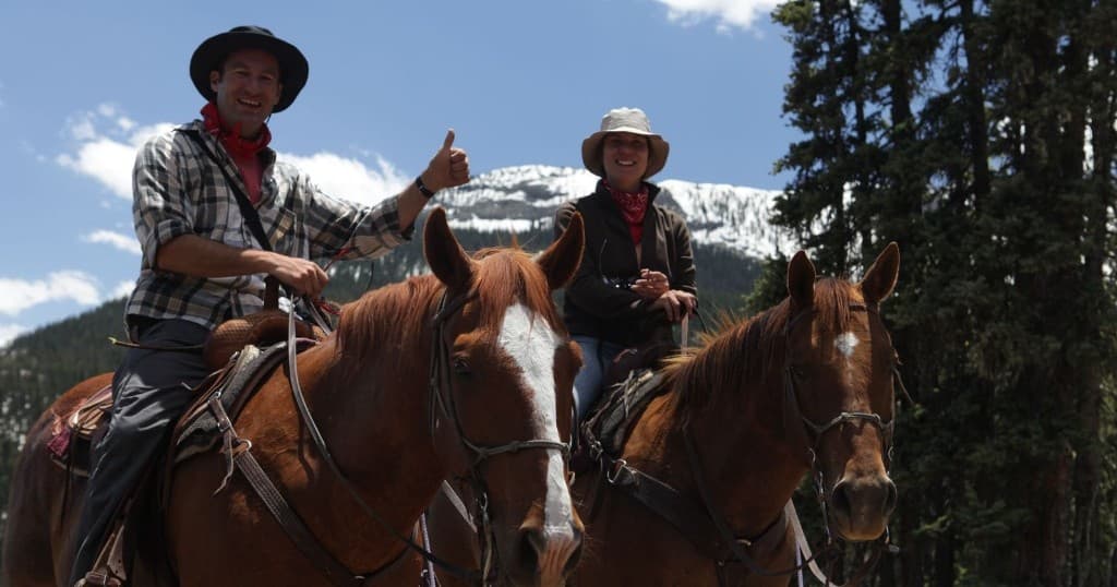 Smiling horseback guides on trail near aspen forests and peaks