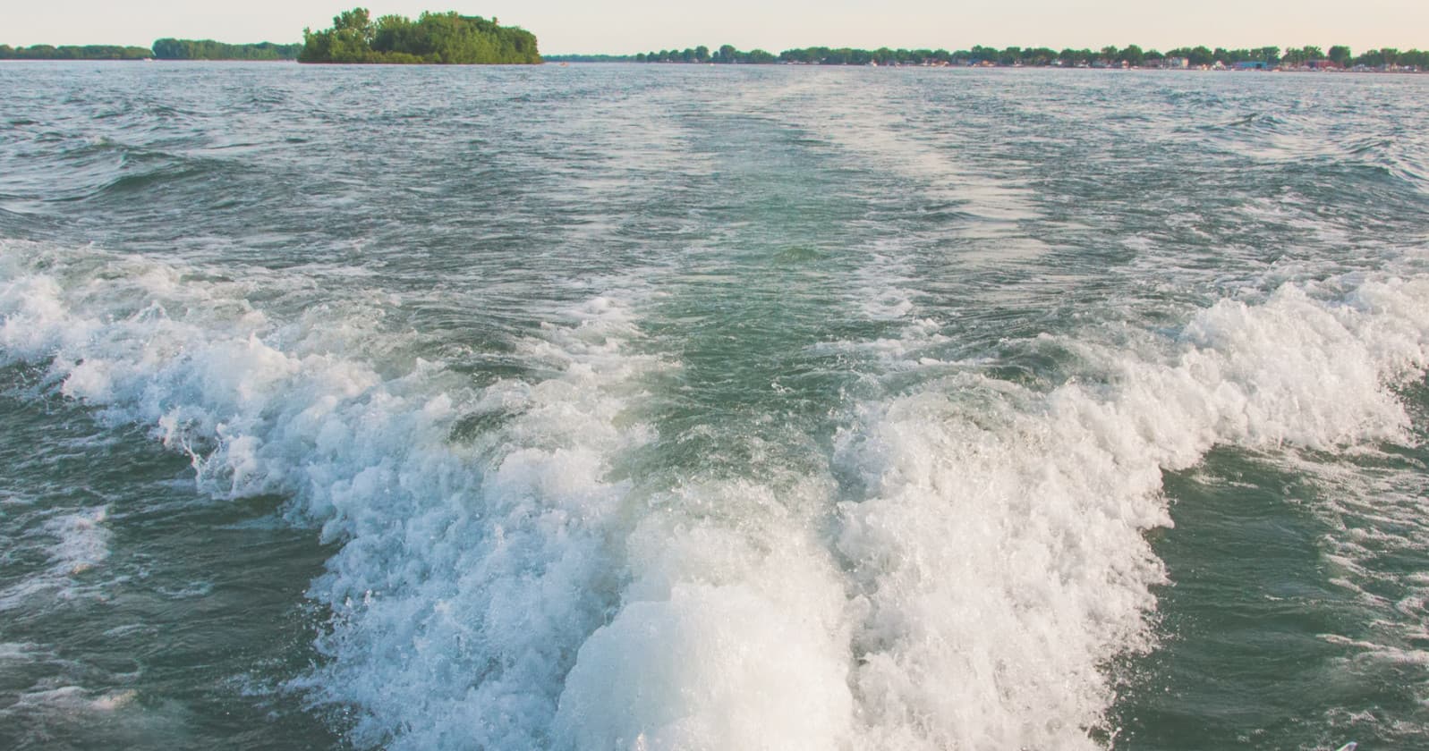 Boat wake trailing across open lake water during day