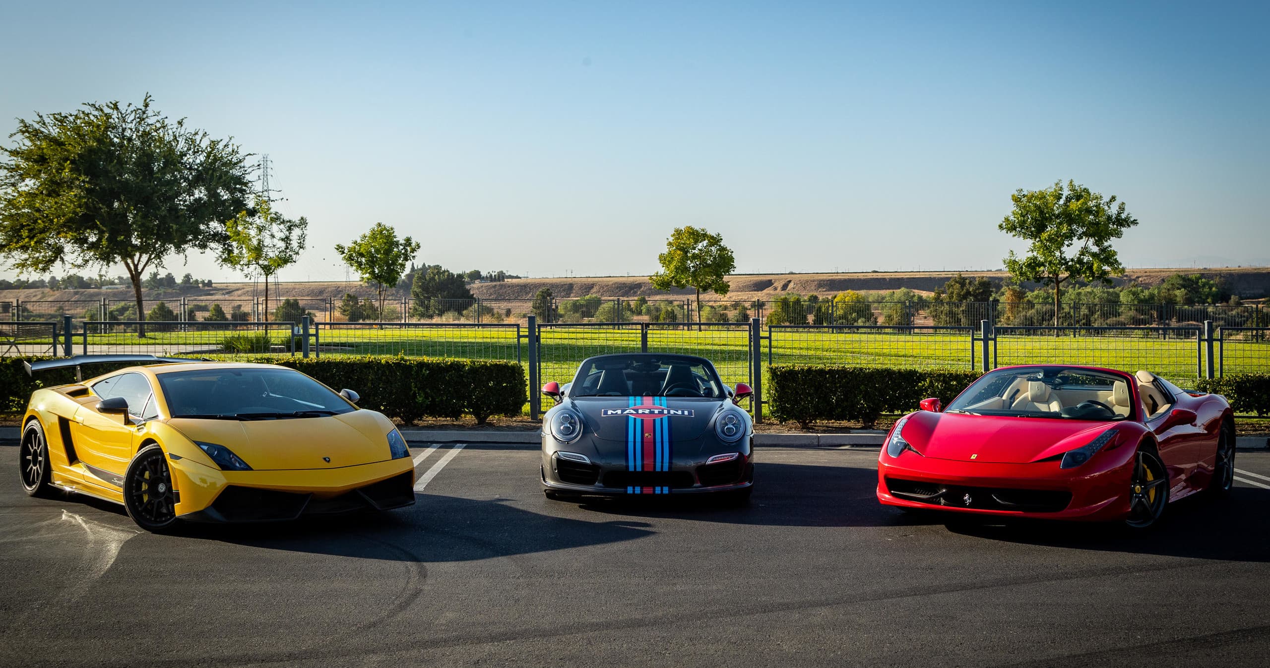 Three exotic cars parked at sunset near open asphalt lot
