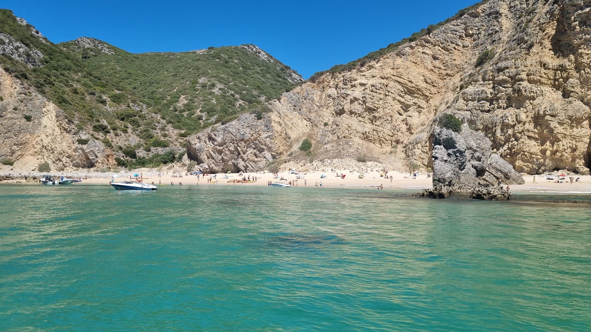 Sandy beach and cliffs with turquoise bay, beachgoers visible