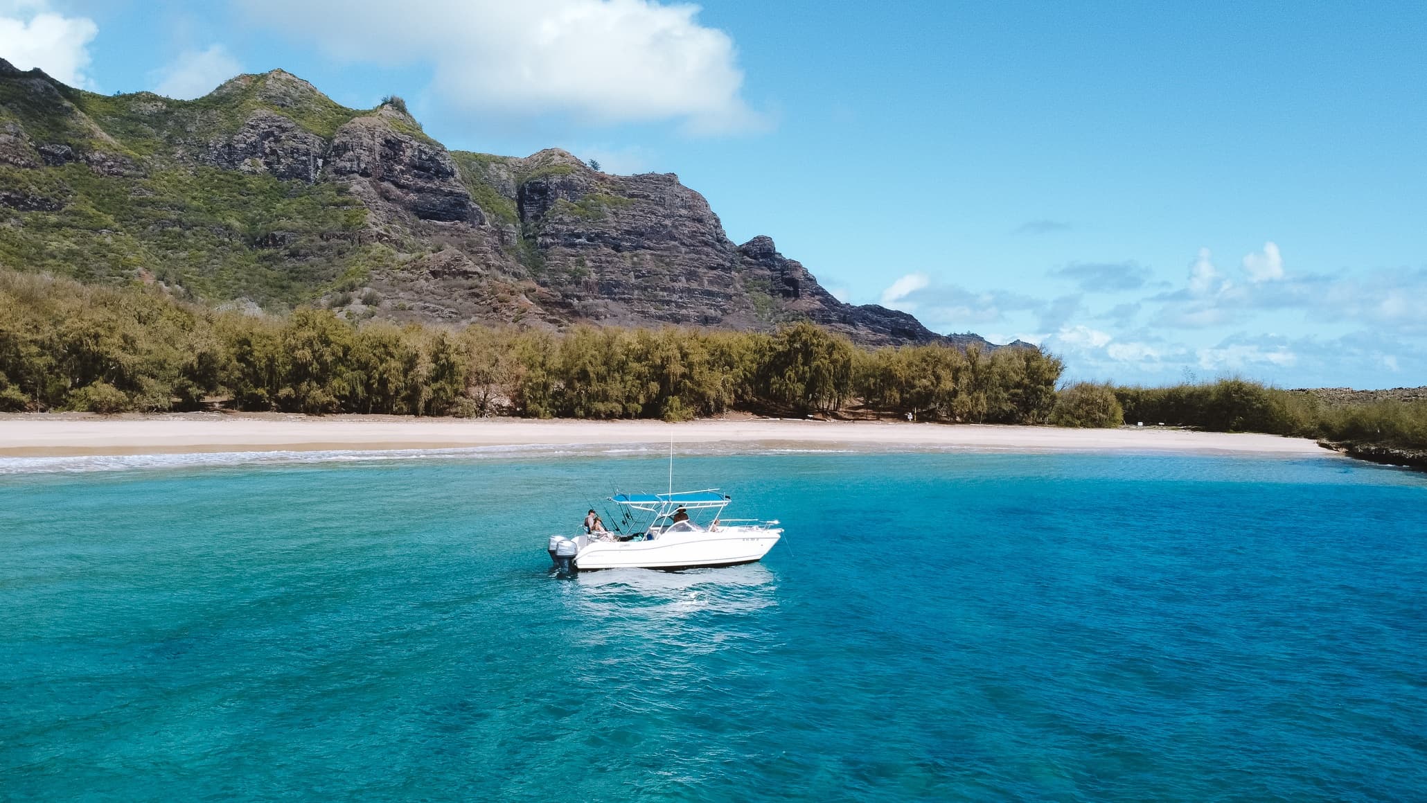Turquoise bay and anchored boat by sandy beach, tropical coastline