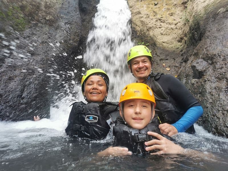 Canyoneering trio wearing helmets under a waterfall in Jalisco