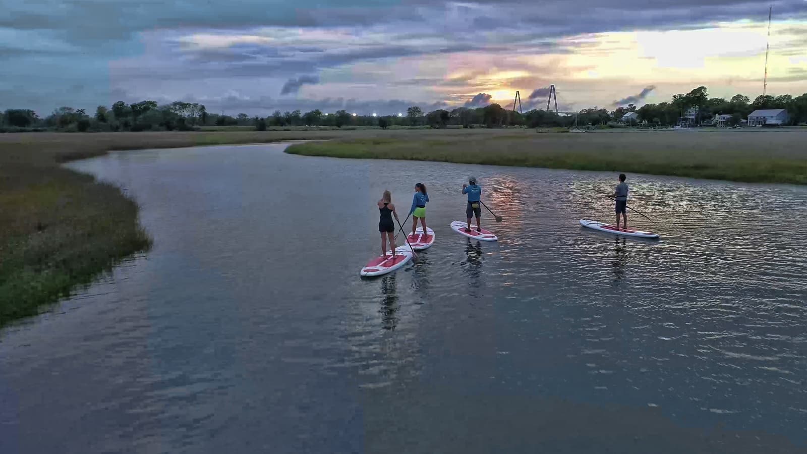 Paddleboarders gliding through marsh estuary at dusk