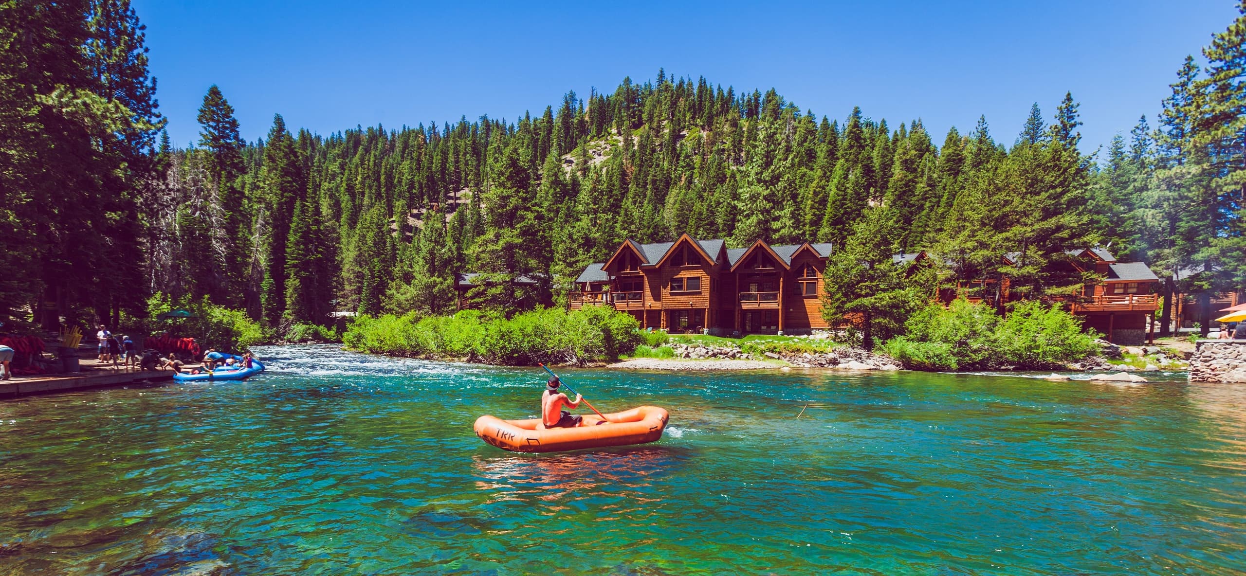 Solo paddler on clear mountain lake near forested cabins