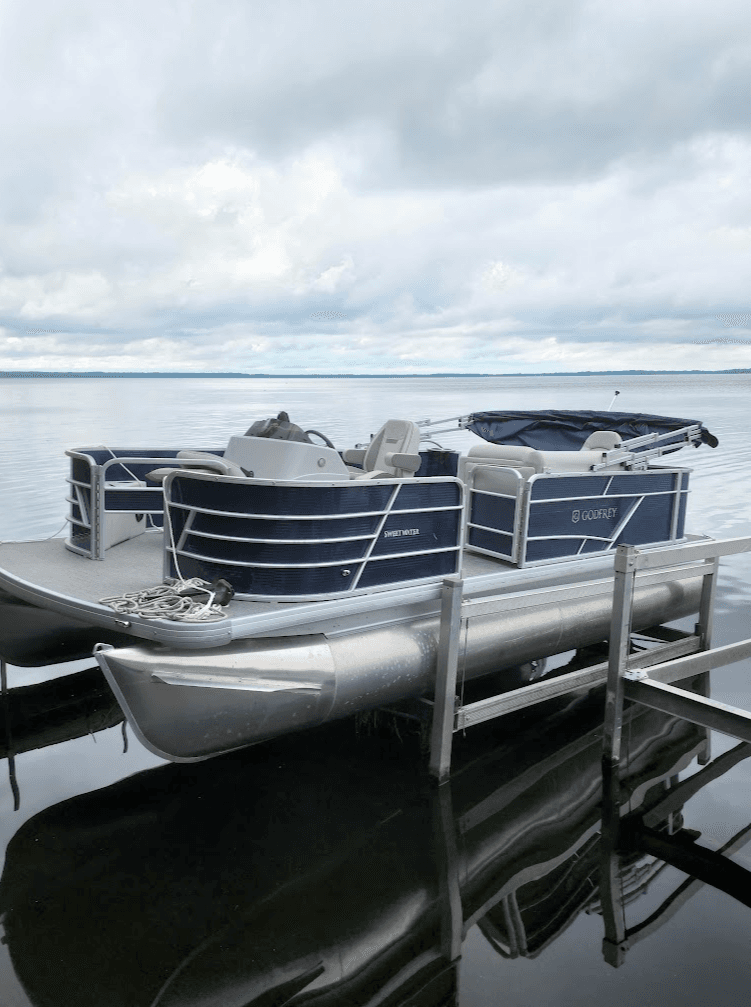 Pontoon boat moored on calm lake with cloudy sky reflection
