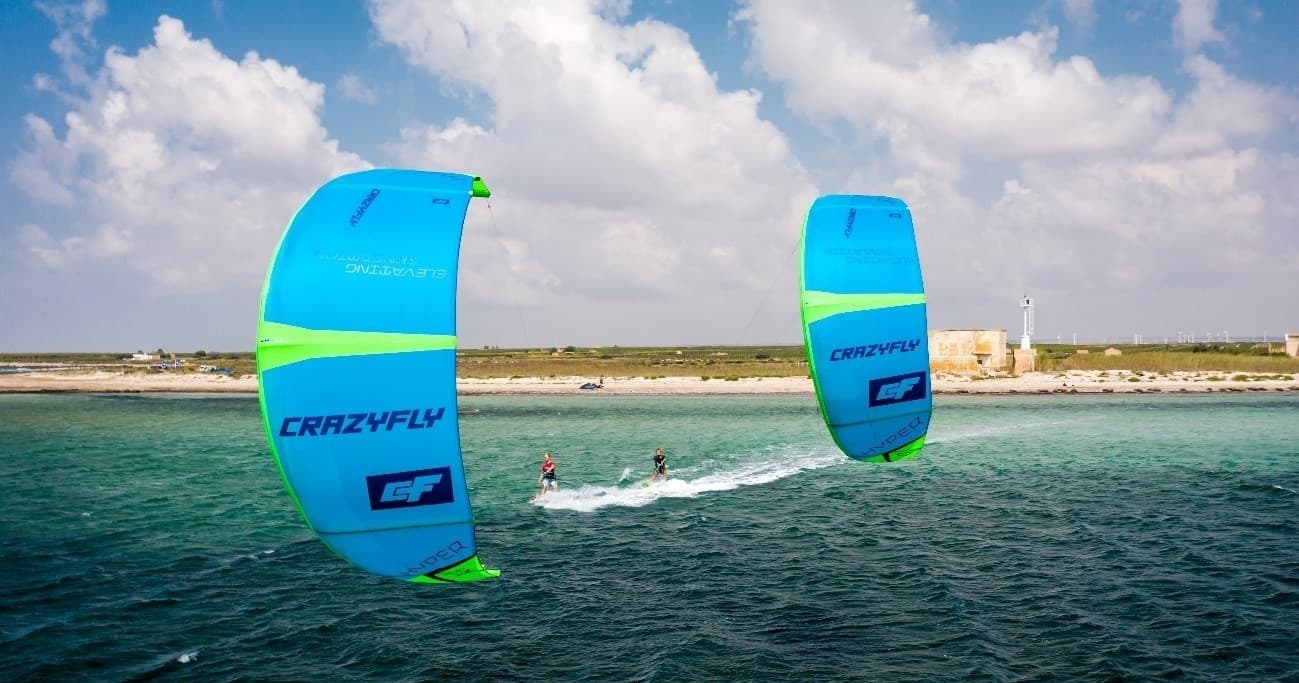 Two kitesurfers skimming turquoise water near a sunny coast
