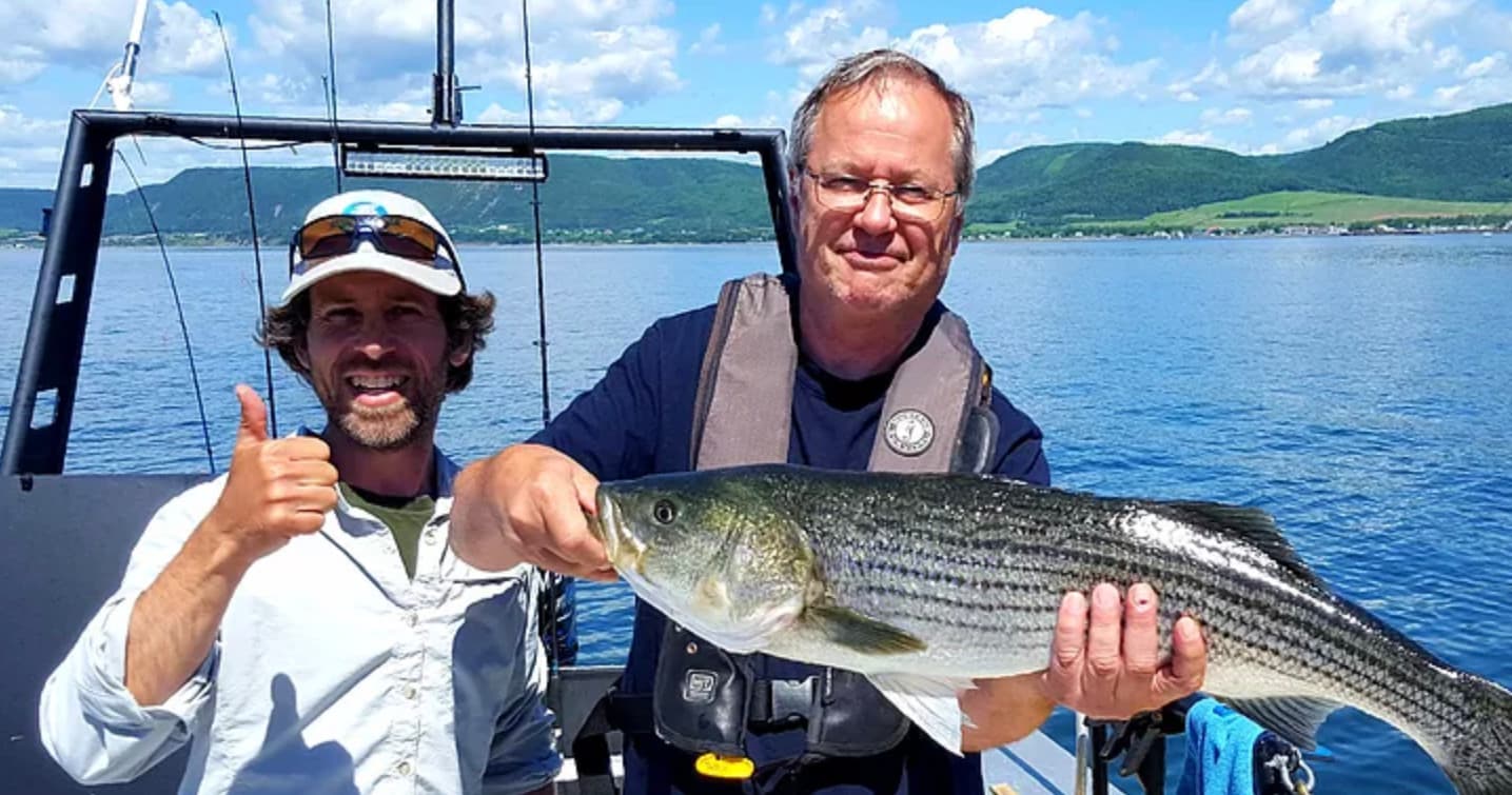 Two anglers displaying a large striped bass on a boat deck