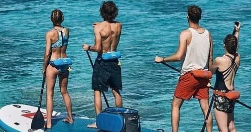 Group paddleboarding on calm ocean near rocky coastline