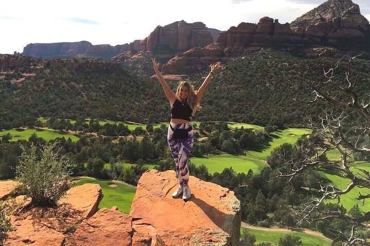 Person standing on red rock cliff overlooking Sedona valley