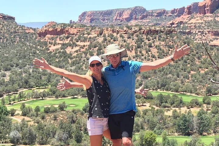 Couple with arms out showcasing Sedona canyon and green valley