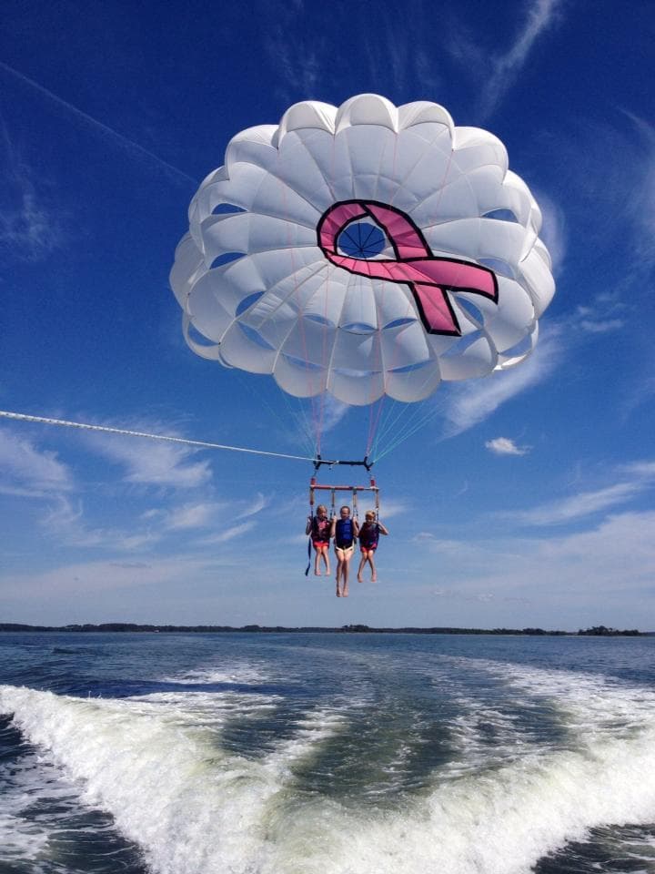 Tandem parasailing trio lifted above open sea with clear sky