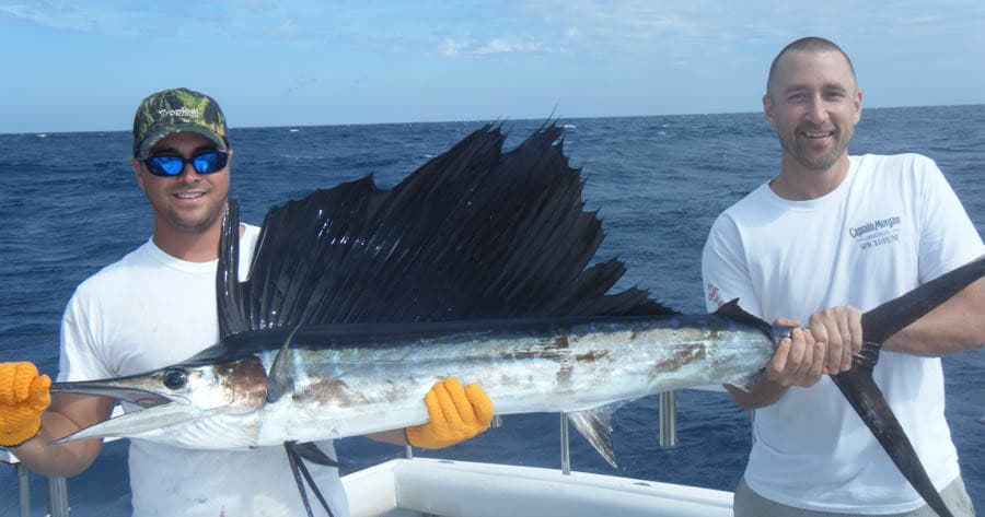 Two anglers holding sailfish offshore in deep sea fishing trip