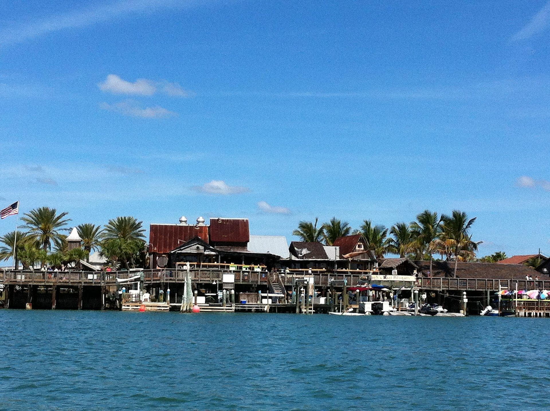 Coastal pier with palm trees and waterfront shops under blue sky