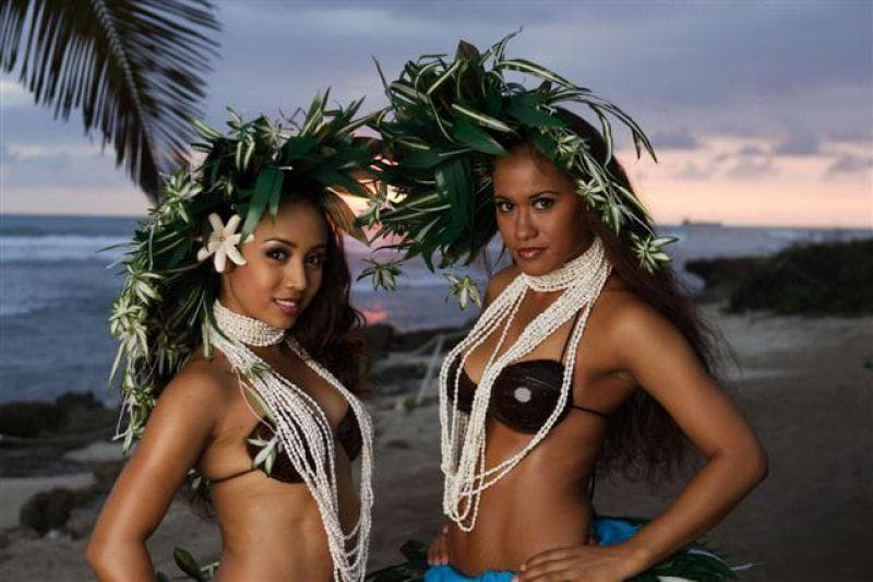 Two hula dancers posing on Hawaiian beach with ocean backdrop