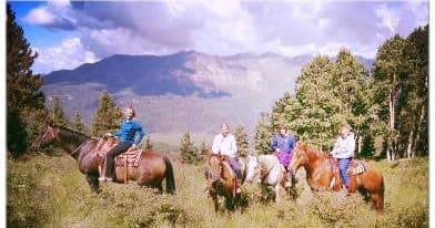 Group horseback riding across alpine meadow with mountain vista