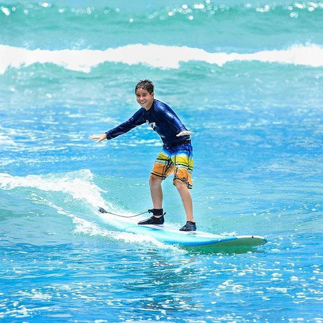 Teen surfing bright turquoise waves near reef, standing on board