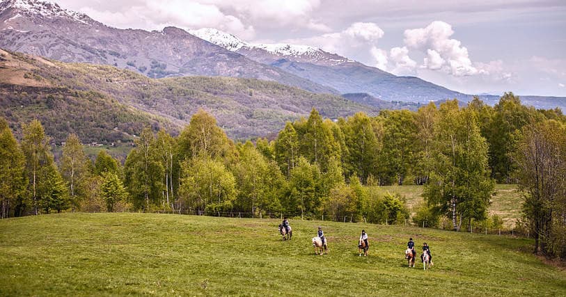 Horseback riders crossing alpine meadow with distant mountain vista