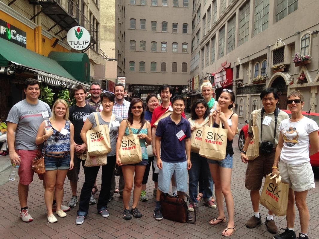 Large walking food tour group on city sidewalk holding tasting bags