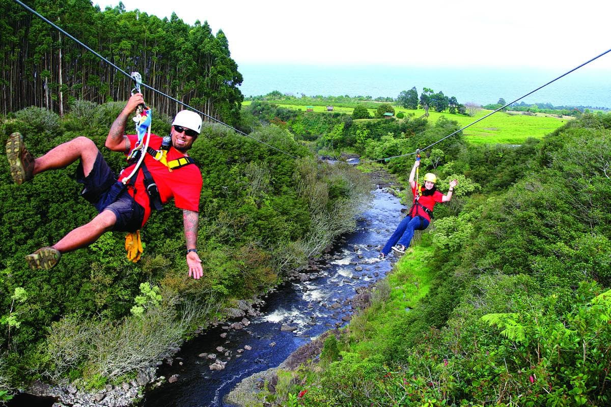 Two zipliners gliding over lush river valley in Hawaii