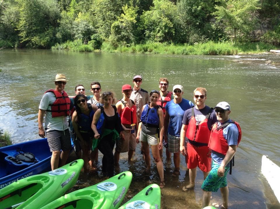Large kayaking group posing on riverbank before paddling trip