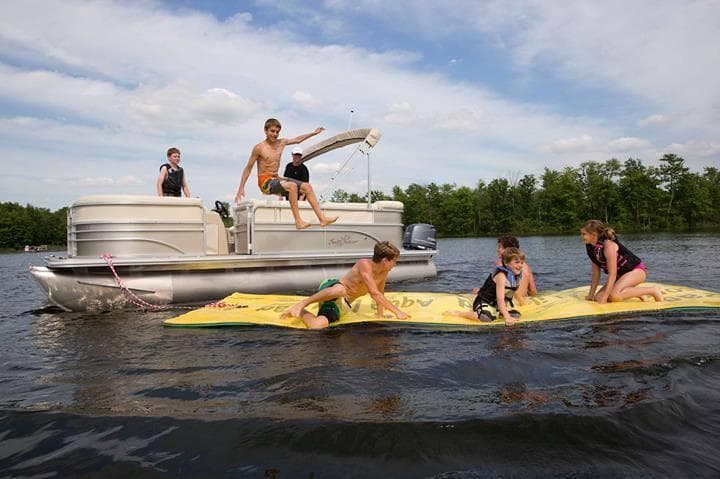 Pontoon and swimmers towing inflatable mat for lakeside fun