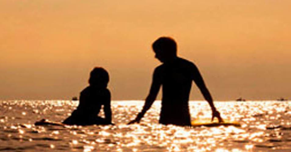 Silhouetted surfers sitting in golden sunset ocean